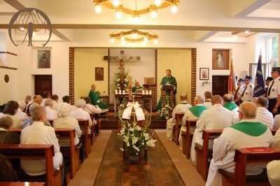 Msza Święta, czyta ks. Andrzej, po prawej stronie Kaplicy stoją poczty sztandarowe OSP, w ławkach siedzą kapłani, z lewej strony w ławkach siedzą Mieszkanki, w centralnym miejscu przed ołtarzem stoi trumna
