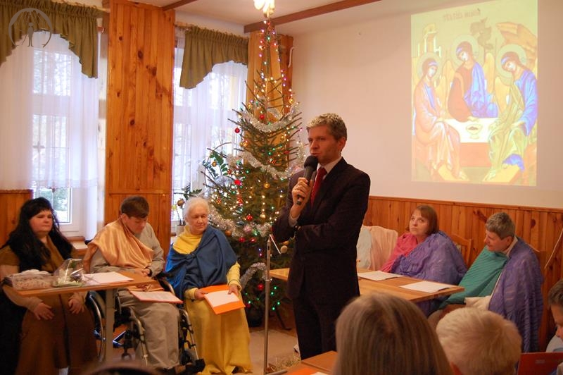 Świetlica Domu Nadziei, pierwszy plan Pan Paweł Kacprzyk Prezes TOnOS mówi przez mikrofon do zebranych, drugi plan scena na której znajduje się Wspólnota Koła Biblijnego