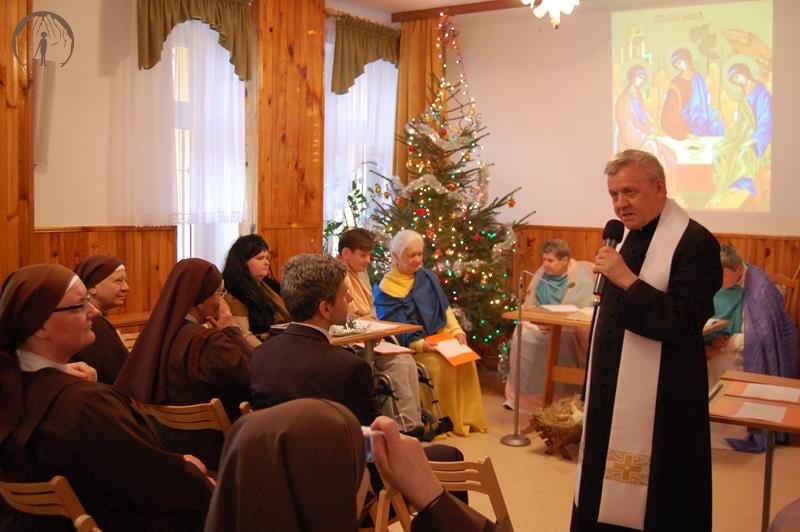 Świetlica Domu Nadziei, pierwszy plan z prawej strony ks. Antoni mówi przez mikrofon do zebranych, z lewej strony uczestnicy spotkania, drugi plan scena na której znajduje się Wspólnota Koła Biblijnego