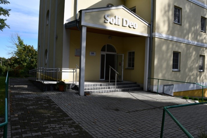 Wejście główne do budynku Soli Deo, trzy schodki z poręczą, z lewej strony rampa podjazdowa
