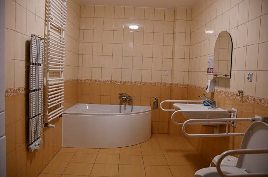 Łazienka w budynku Soli Deo, narożna wanna, przy umywalce i sedesie zamocowane poręcze