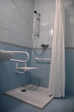Łazienka w budynku Soli Deo, poręcze przy umywalce, poręcze i rozkładane siedzisko w płaskim brodziku
