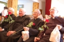 Świetlica w Domu Nadziei, od lewej siedzą uśmiechnięci ks. Stanisław, ks. Andrzej, ks. Antoni i ks, Czesław, wszyscy trzymają w ręku czerwoną różę oraz upominek
