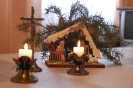 Świetlica na jednym ze skrzydeł, na stole stoją dwie zapalone świece, drugi plan Krucyfiks i bożonarodzeniowa szopka
