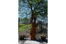 Pobocze drogi do Domu Nadziei, drewniana kapliczka z figurą Matki Bożej Niepokalanej stojąca na postumencie z pnia drzewa, w tle kwitnące drzewo.