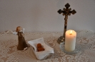 Ołtarzyk kolędowy, krucyfiks, zapalona świeca,  Anioł stoi przy Dzieciątku Jezus leżącym w żłóbku