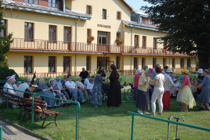 Ogród przed Domem Nadziei, Mieszkanki i Uczestnicy WTZ  tańczą i odpoczywają na ławkach w cieniu rozłożystej lipy