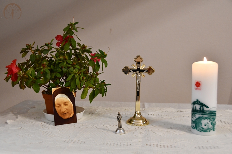 Ołtarzyk kolędowy, krucyfiks, zapalona świeca, figura św. Józefa trzymającego Dzieciątko Jezus, obraz bł. Matki Elżbiety, kwiat