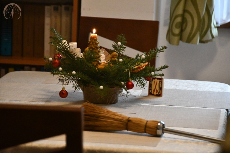 Stroik świąteczny z zapaloną świecą, obok leży kropidło